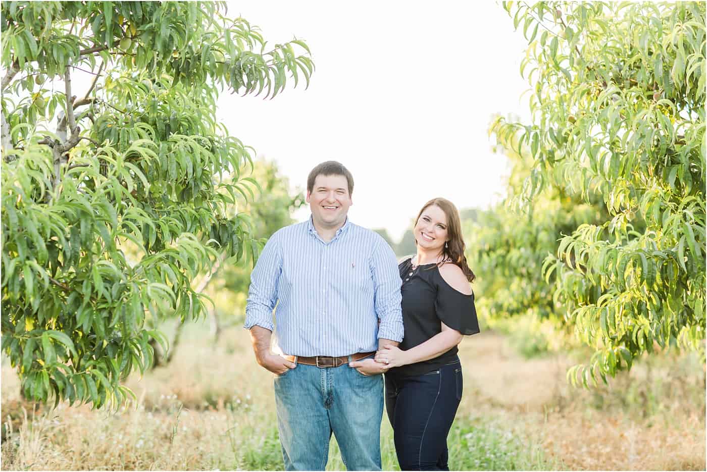 bride and groom standing for engagement photos in a peach orchard photographed by youngstown wedding photographer