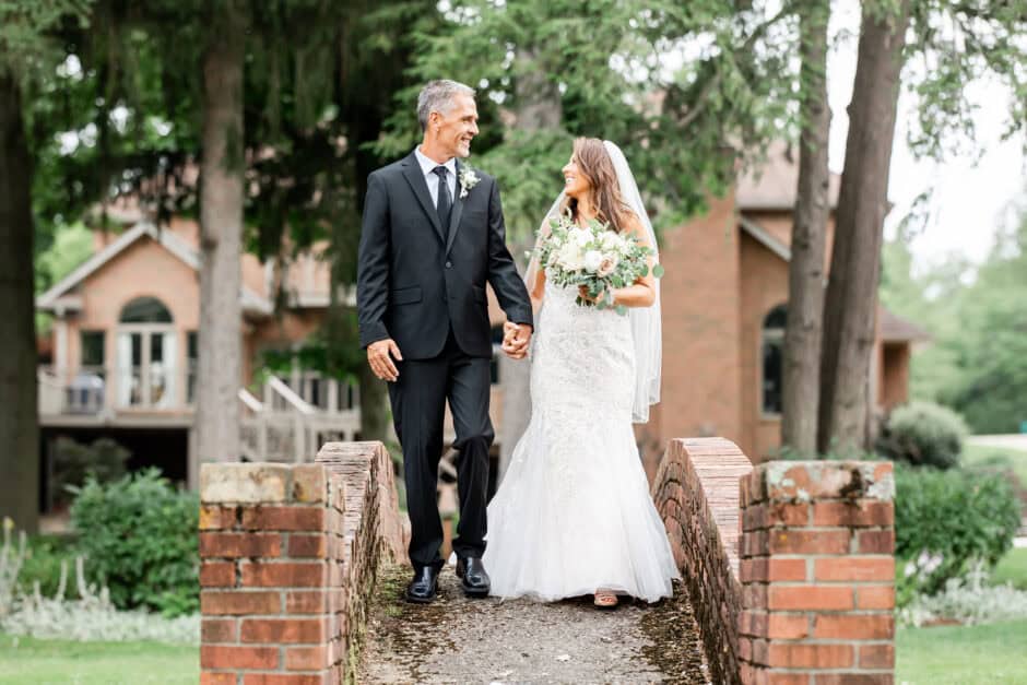 Bride and groom walking together across a brick bridge at Glenmoor Country Club, captured by Loren Jackson Photography for couples planning weddings after visiting Cleveland Ohio bridal shops.