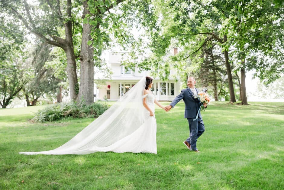 Bride and groom walking across a grassy lawn with flowing cathedral veil at Nature Valley Lodge, photographed by Loren Jackson Photography for couples exploring Cleveland Ohio bridal shops