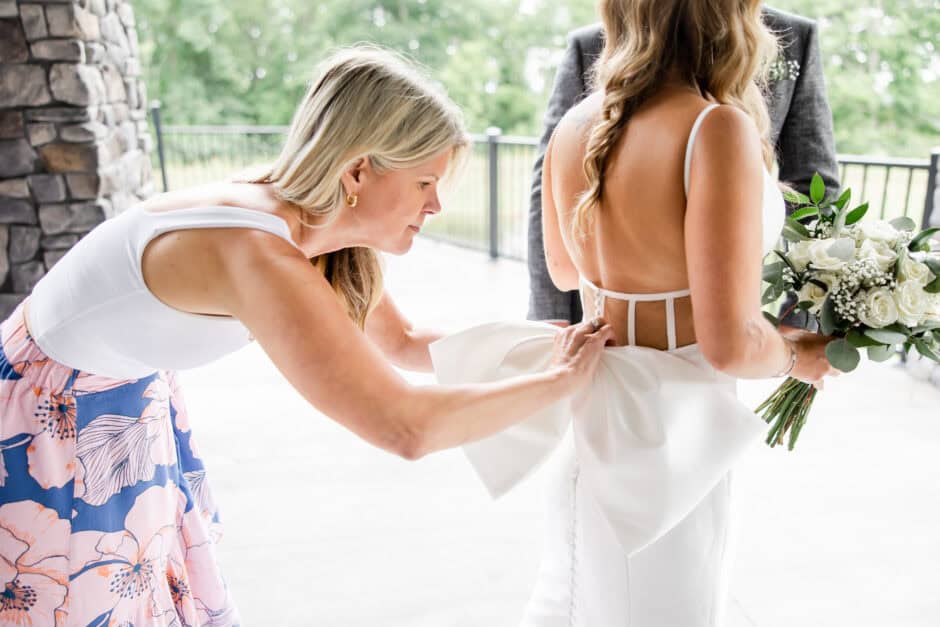 Wedding planner assisting bride with dress bustle at The Reserve at Stonecreek, behind-the-scenes moment captured by wedding photographer Cleveland OH with Something Pink Planning